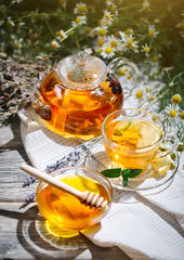 Cup with hot tea with mint and a thyme on a wooden table in a summer garden.
