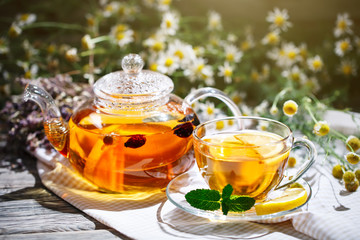Cup with hot tea with mint and a thyme on a wooden table in a summer garden.