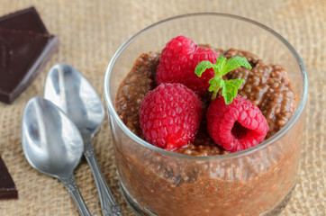    Raw vegan dessert background. Sugar free Carob  Chia Pudding  with almond milk and raspberries in glass on wooden table. Healthy eating concept.