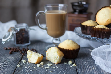 Lot of whole cupcakes and pieces on wooden table, next to glass cup with cappuccino