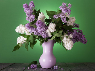Bouquet of blue and white lilac in vase on green background