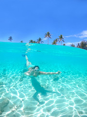 HALF UNDERWATER: Woman snorkels towards the camera and makes the ok gesture.