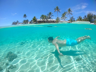 Fototapeta na wymiar HALF UNDERWATER Active young man swims along the breathtaking exotic sandy shore
