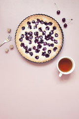 Whole homemade cherry cake on pastel pink background with fresh berries and cup of tea.
