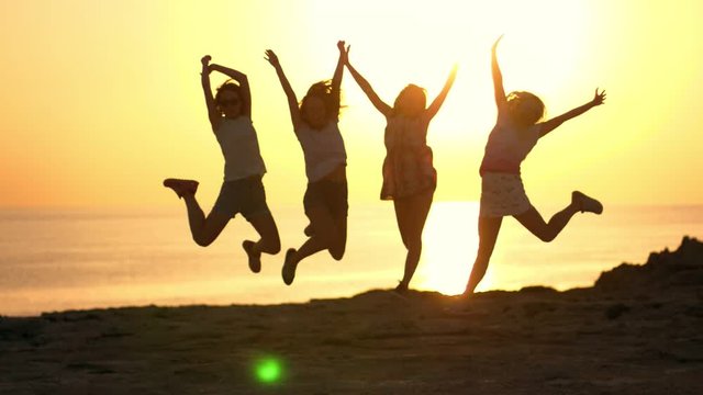 Silhouettes of happy friends jumping at beach sunset. People silhouettes jumping on background of sunset sky. Joyful girls enjoy summer vacation. Summer girls silhouette jump at beach