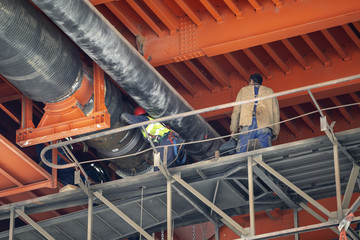 Workers welding district heating pipeline under metal bridge