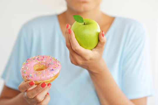 Young woman choosing to eat a healthy green apple fruit instead of attractive hyper caloric donut
