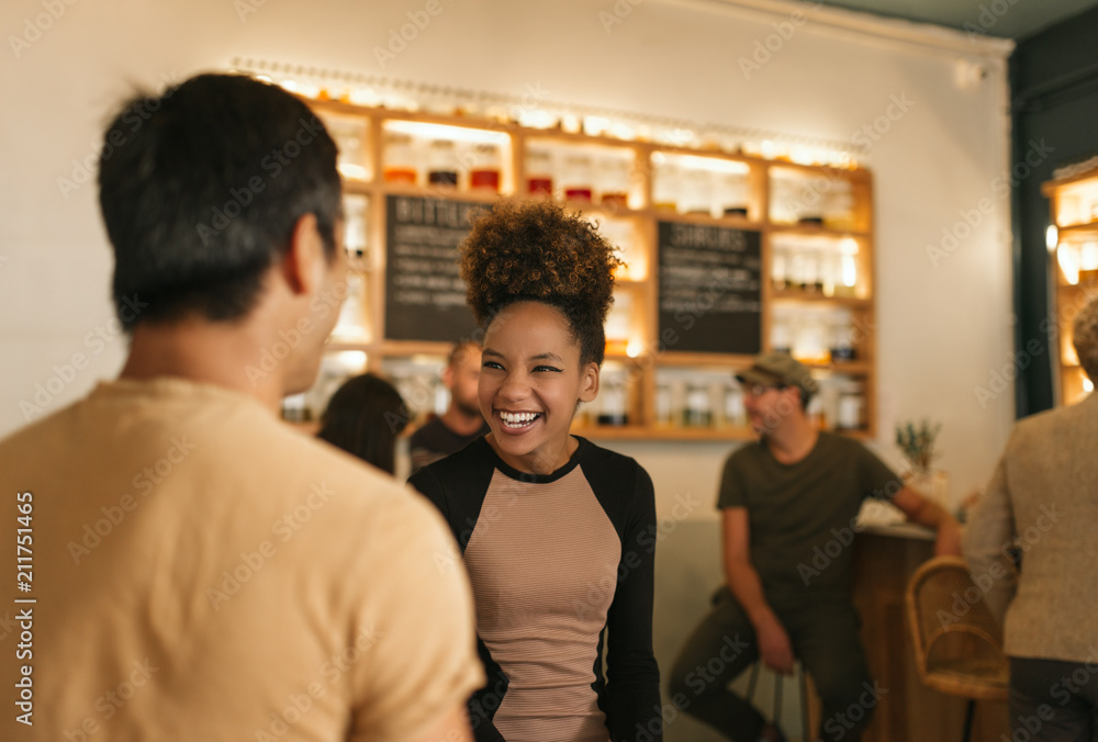 Wall mural Laughing young woman talking with her friend in a bar