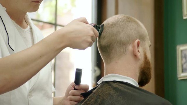 Barber making haircut for young redhead man with a beard in a barber's. 4K