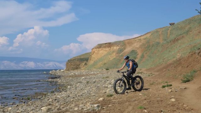 Fat bike also called fatbike or fat-tire bike in summer driving on the beach. The guy is riding heavily to the stony bank. The stones are big. The picture is contrast.