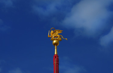 Fototapeta na wymiar Saint Mark Winged Lion golden statuette wielding a sword against blue sky, a symbol of the Old Venice Republic at war