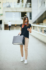 Woman holding shopping bags and using smart phone in front of shopping mall.