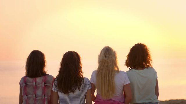 Back view of sitting woman enjoy beach sunset. Four young girls watching sunset in slow motion. Women on tropical vacation enjoying sunset at sea. Enjoy summertime. Female lifestyle on Cyprus vacation