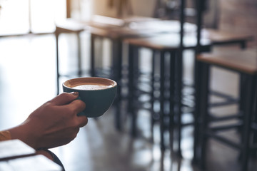 Closeup image of a hand holding a cup of coffee in cafe