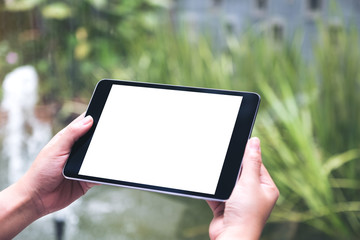 Mockup image of hands holding black tablet pc with white blank desktop screen with green nature background