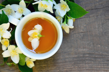 Jasmine tea in a white cup with fresh jasmine flowers on old wooden table.Healthy drink,diet or herbal medicine concept.Top view.Copy space.Selective focus.