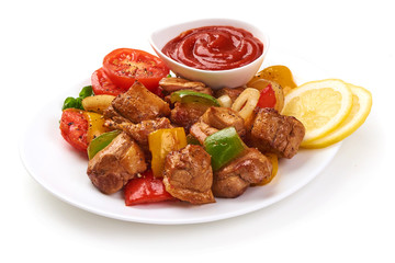 Pieces of grilled barbecue with vegetables and tomato sauce on plate, isolated on white background. Close-up