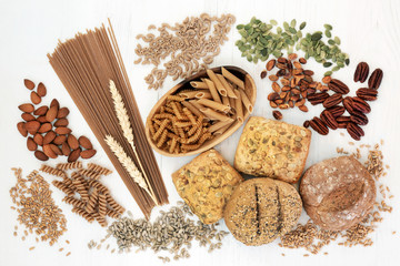 High fiber health food with whole grain bread rolls, whole wheat pasta, nuts, seeds and grains. Rustic background on wood, top view. Foods high in omega 3, antioxidants and vitamins.