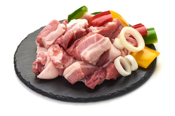 Pieces of fresh pork meat sliced vegetables on stone plate, isolated on white background. Close-up.