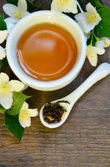 Jasmine dry green tea leaves in a spoon with jasmine flowers and cup of tea on old wooden background.Healthy drink,diet or herbal medicine concept.Top view.Selective focus.