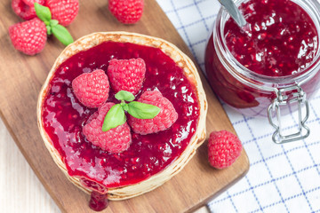 Stack of pancakes or fritters with raspberry jam and berries on a wooden board, horizontal, top view