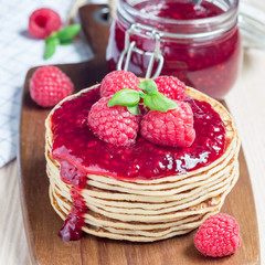 Stack of pancakes or fritters with raspberry jam and berries on wooden board, square