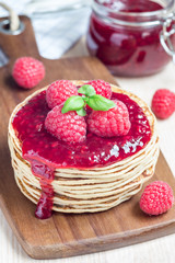 Stack of pancakes or fritters with raspberry jam and berries on a wooden board, vertical
