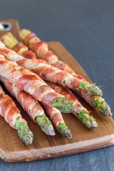 Green asparagus wrapped with bacon on wooden board, vertical, copy space