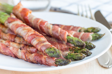Green asparagus wrapped with bacon on white plate, horizontal