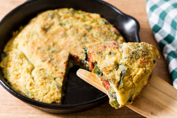 Frittata made of eggs and vegetables in a iron pan, on wooden table.