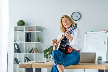 smiling beautiful businesswoman playing acoustic guitar in office
