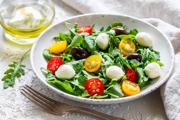Fototapeta na wymiar Fresh summer salad with arugula, yellow and red cherry tomatoes, Kalamata olives and mozzarella