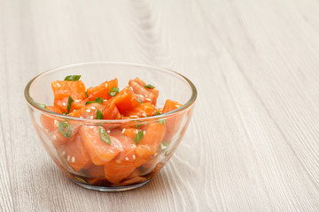 Hawaiian salmon poke with green onions and sesame seeds in glass bowl