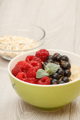 Oatmeal porridge in porcelain bowl with currant berries and raspberries, decorated with mint leaves