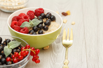 Oatmeal porridge in porcelain bowl with currant berries and raspberries, decorated with mint leaves