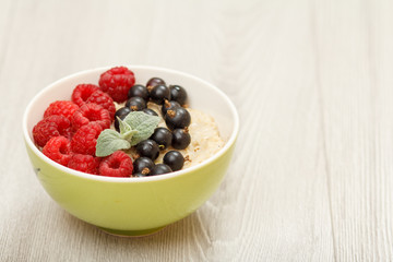 Oatmeal porridge in porcelain bowl with currant berries and raspberries, decorated with mint leaves