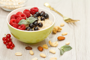 Oatmeal porridge in porcelain bowl with currant berries and raspberries, decorated with mint leaves