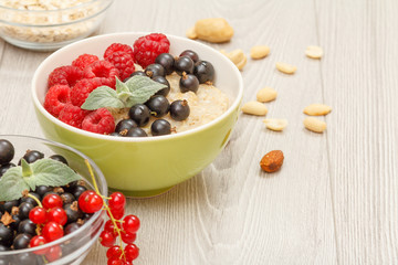 Oatmeal porridge in porcelain bowl with currant berries and raspberries, decorated with mint leaves