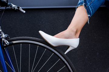 cropped image of woman in white shoe touching bike wheel on street