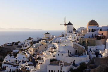 Fototapeta na wymiar Famous stunning view of white architectures and windmills above the volcanic caldera in the village of Oia in Santorini island, Greece