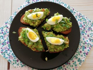 Healthy tasty fresh lunch of homemade guacamole and boiled egg on brown toast served on a black plate