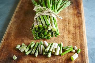top view of bunch of fresh raw garden asparagus on rectangular wooden cutting board on gray concrete background. Ingredients for cooking. Food background.