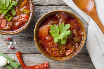 Borsch, beetroot soup in a wooden bowl with fresh herbs on a wooden background.