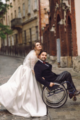 Bride and groom on the wheelchair pose on old European street