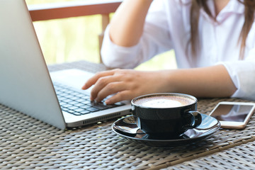 Young business woman sitting at table in coffee shop. On table is laptop, smartphone and cup of coffee.