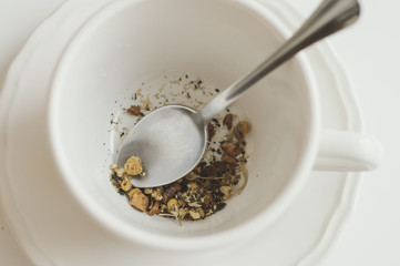 Dry herbal tea with camomile in white cup and metal spoon. Healthy drink