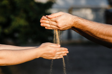 The sand is poured out of the hands of men into women's hands.