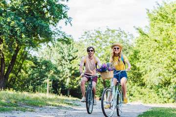 young couple riding retro bicycles in park on summer day