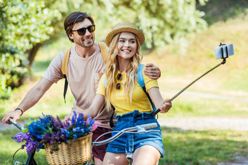 smiling couple in love with bicycles taking selfie in park on summer day