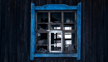 Old dark broken window in Russia with blue leaf